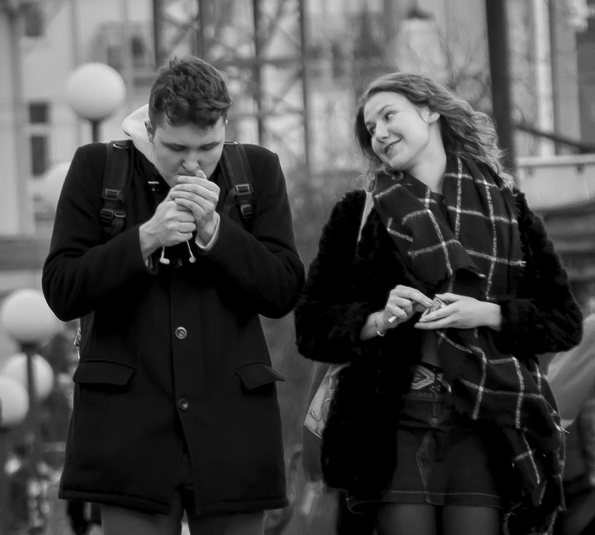 Young man lighting a cigarette while a woman beside him watches
